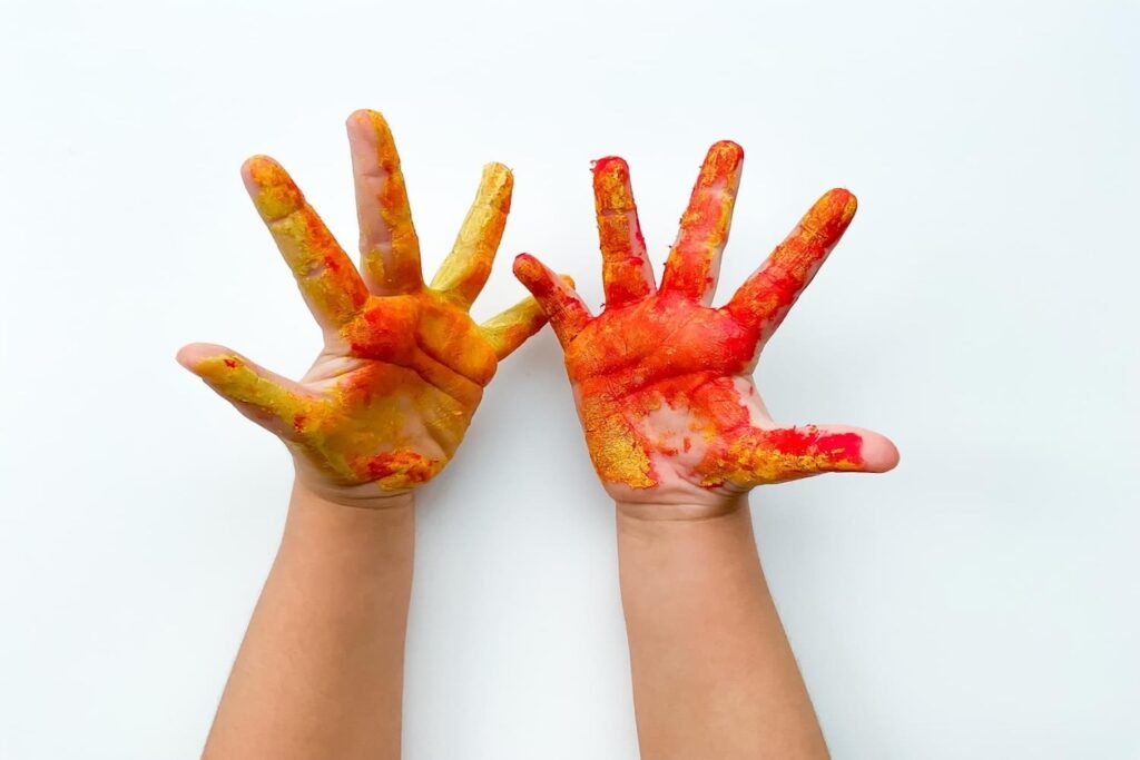 Kid with red and yellow paint on hands - Childcare Consultant in Sydney